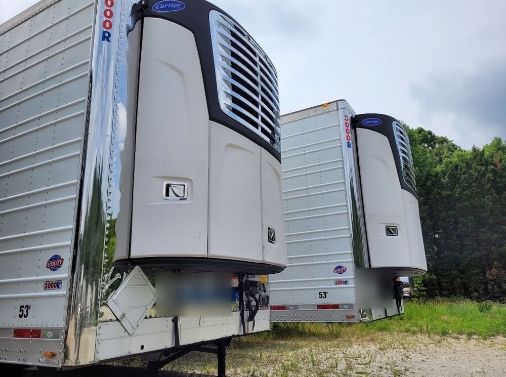 Two refrigerated trailers with Carrier reefer units on the nose, parked on gravel
