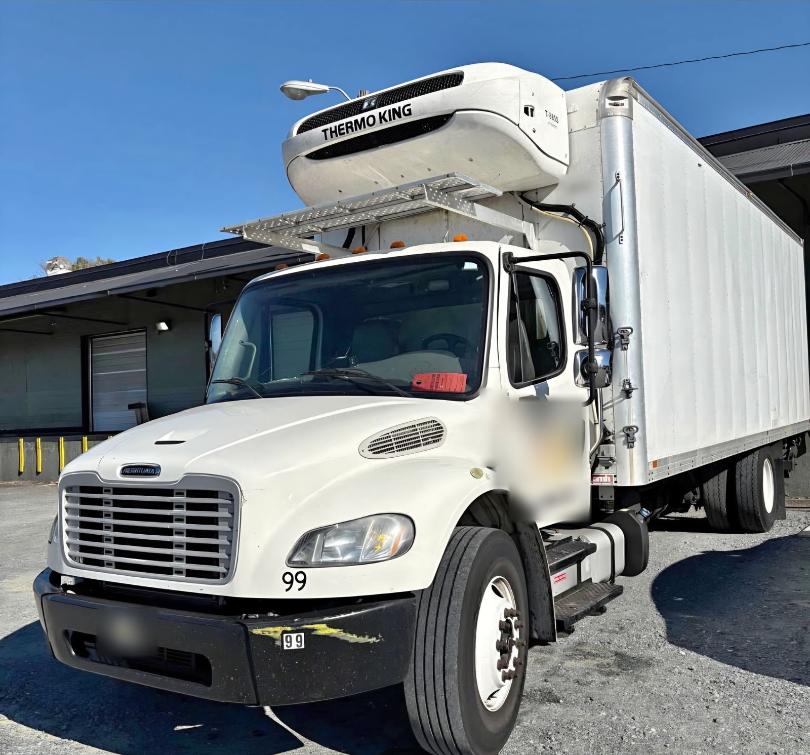 White box truck with a Thermo King refrigeration unit mounted above the cab, parked at a loading dock